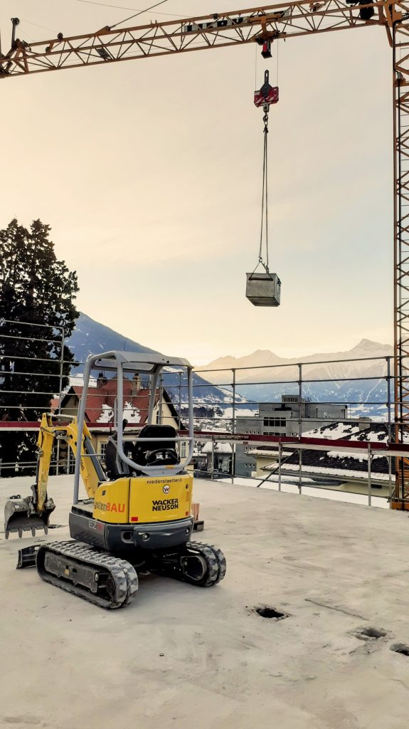 Das Bild zeigt einen kleinen Bagger auf  der Ebene des abgetragenen Dachgeschosses des FinKa Hostel. Hier befindet sich heute das Stockwerk mit den Rooftopzimmern mit Terrasse.