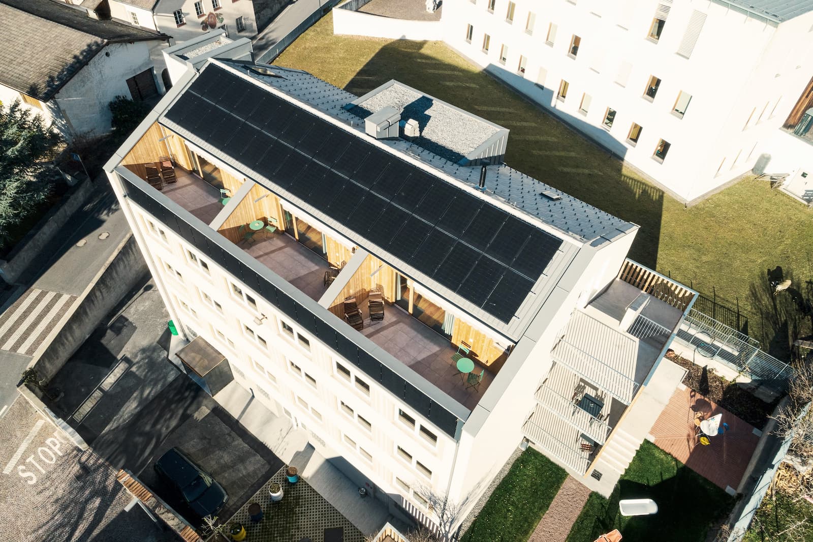 Luftaufnahme der FinKa in Mals mit modernem Dachgeschoss, Photovoltaikanlage und Terrassen – Umbau der ehemaligen Finanzkaserne zu einem nachhaltigen Hostel.